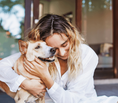 Lady in blondie hair and white long shirt hugging a dog